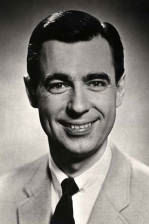 A headshot of a white man, Mr. Rogers, wearing a suit and staring directly