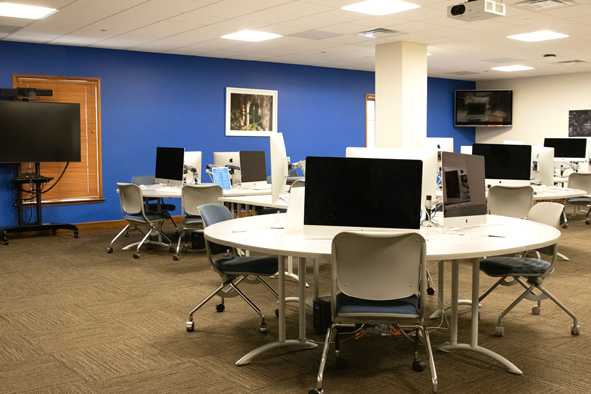 a bank of Mac computers sitting atop circular desks, with gray chairs with blue cushions tucked underneath